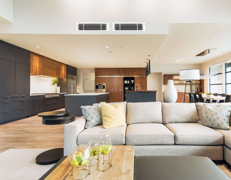 Modern open-plan living space with a light-colored sofa, wooden coffee table, and kitchen area