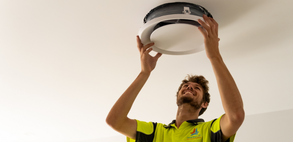 A person in a yellow high-visibility shirt installing a circular ceiling fixture