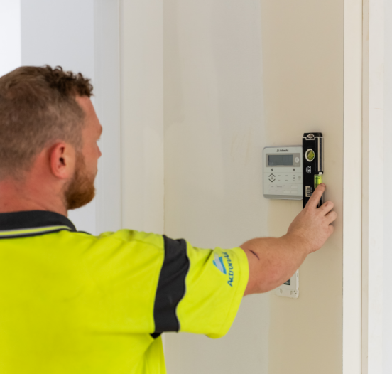 A man in a high-visibility shirt using a spirit level to check the alignment of a control panel