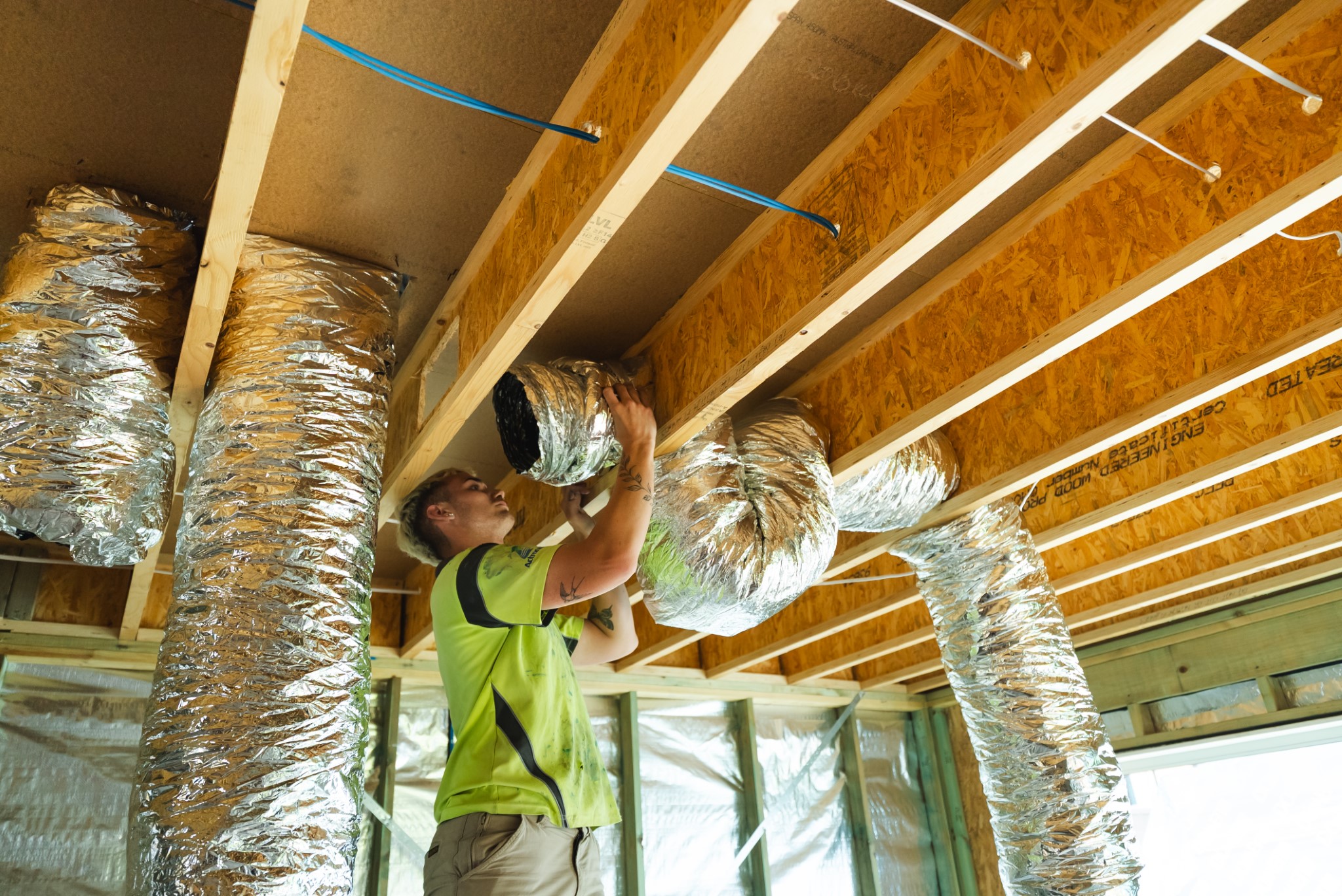 Person installing flexible HVAC ductwork in the ceiling of a house under construction